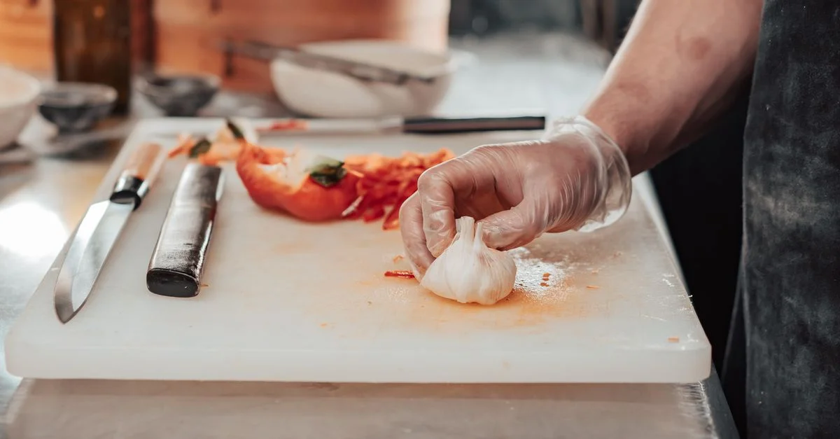 Un chef prépare des ingrédients, y compris de l'ail, sur une planche à découper avec des couteaux à portée de main.