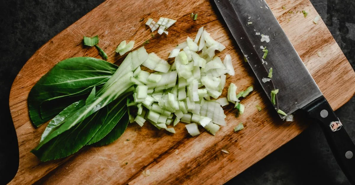 Gros plan de bok choy haché sur une planche en bois avec un couteau, parfait pour des concepts de cuisine saine.