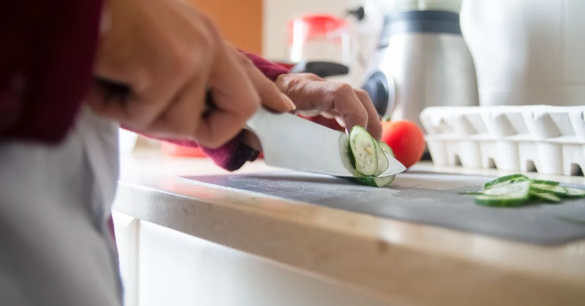 Gros plan sur une personne tranchant des concombres sur un plan de travail de cuisine pour une préparation de repas saine.